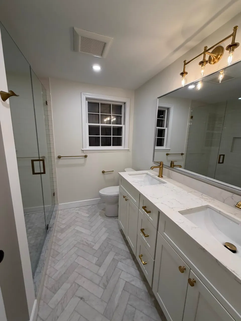 After: finished bathroom with glass shower, herringbone marble floor and double vanity