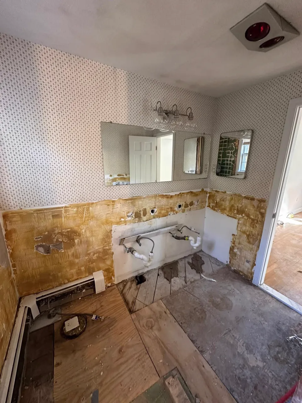 Before: bathroom stripped to the subfloor with old wallpaper and plumbing exposed