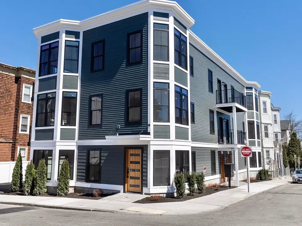 Three-story corner multifamily building with navy and gray siding, black windows and a wood entry door
