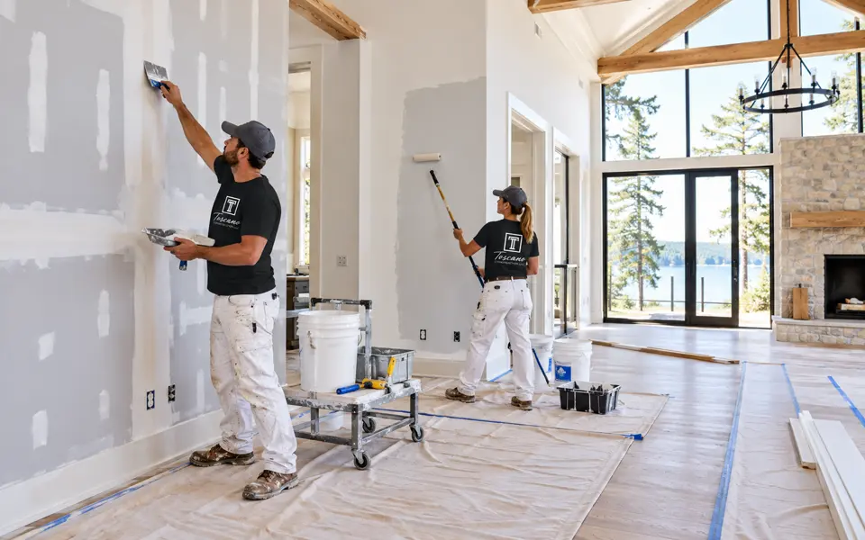 Toscano crew finishing drywall and rolling paint in a bright great room, floors protected